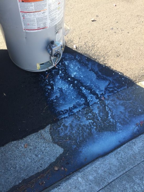 cloudy water caused by calcium buildup is being drained from a recently removed water heater on the side of the street