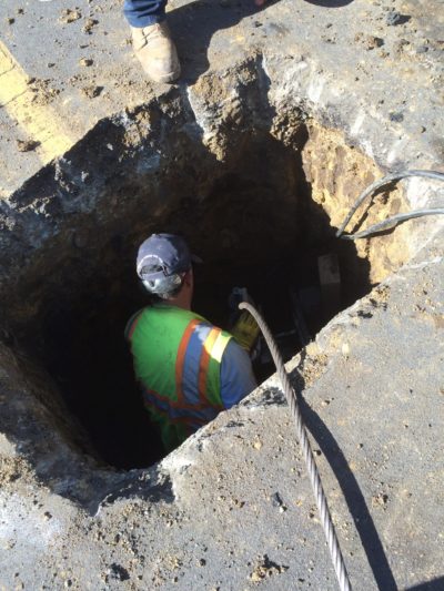 entry point for trenchless being dug in the street with gas line repair technician inside sewer repair